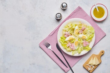 Parisian salad of lettuce, boiled potatoes, ham, and hard-boiled eggs in a light-colored plate against a gray concrete background.