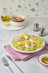 Parisian salad of lettuce, boiled potatoes, ham, and hard-boiled eggs in a light-colored plate against a gray concrete background.