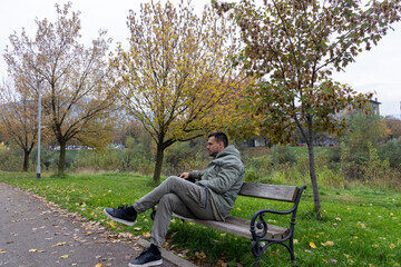 Fototapeta premium Man resting alone on a bench in a park during autumn, surrounded by colorful trees and fallen leaves, symbolizing peace, solitude, and reflection in a calm natural environment.
