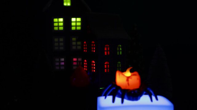 A candle in a spider candlestick on a white stand moves against the backdrop of a Halloween village with black houses