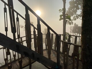 grassy mountain slope with a wooden fence, lit by morning sun. Tall evergreen overlooks hazy valleys. moody winter sunset over the Cotswold countryside. Sunlight on the morning with sea of fog.