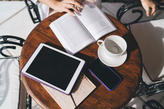 Close-up of freelancer workspace with tablet, book and coffee. Scene reflects slow productivity, digital reading and hybrid workflow between technology and analog habits.