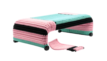 A low rectangular stool with colorful knitted panels and a detached section, set against black