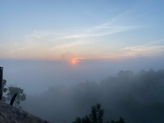 grassy mountain slope with a wooden fence, lit by morning sun. Tall evergreen overlooks hazy valleys. moody winter sunset over the Cotswold countryside. Sunlight on the morning with sea of fog.