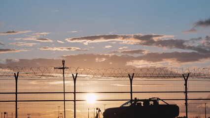 Airport security patrol driving along perimeter fence at sunset