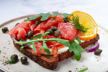 sandwich with freshly smoked salmon, on black bread, with cottage cheese, with herbs and red onions, capers and pieces of citrus fruits, on a marble countertop, breakfast, no people,