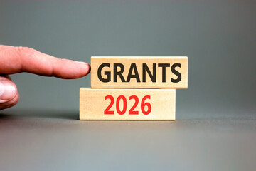 Grants 2026 symbol. Concept words Grants 2026 on beautiful wooden blocks. Beautiful grey paper background. Businessman's hand. Business and grants 2026 concept. Copy space.