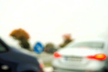 Abstraktes Motiv mit silberweißem Auto vor blauem Auto beim Fahren durch Kreisel mit blauem Richtungsschild und Bäumen vor weißem Himmel bei Regen und Sturm im Herbst