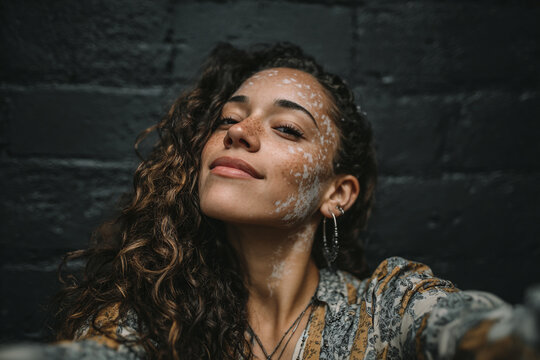 Confident curvy mixed-race woman with vitiligo taking a selfie on a white background. Concept of self-love, diversity, and body positivity.