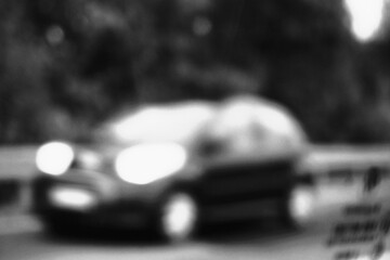 Abstraktes Schwarz-weiß Motiv mit schwarzem Auto und weißen Lichtern fährt auf Straße vor Leitplanken und Bäumen auf Landstraße am Nachmittag im Herbst