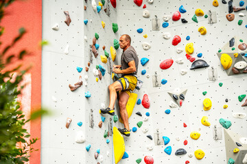 Athletic Man Climbing Indoor Rock Wall: Focused Climber Scaling Colorful Artificial Holds In Modern...