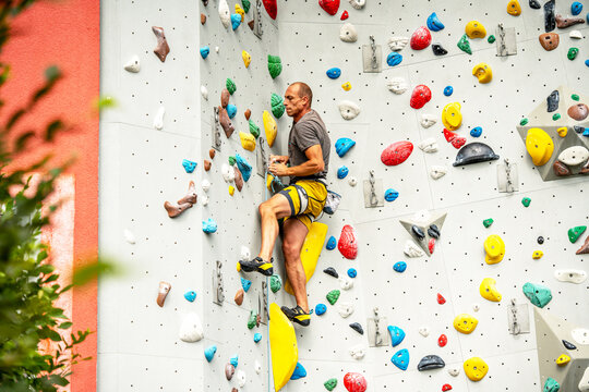 Athletic Man Climbing Indoor Rock Wall: Focused Climber Scaling Colorful Artificial Holds In Modern Climbing Gym With Strong Light And Dynamic Angles