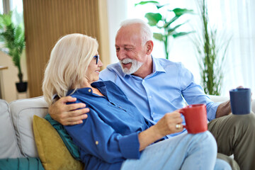 Obraz premium Portrait of a happy senior couple embracing talking and drinking coffee or tea at home