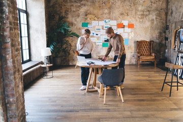 Young freelancer team deeply engaged in planning session, reviewing hand-drawn charts and digital...