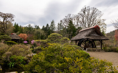 Beautiful garden with traditional thatched roof structure in a serene landscape during cloudy weather