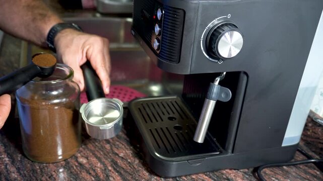 A person puts ground coffee into the espresso machine's dispenser.