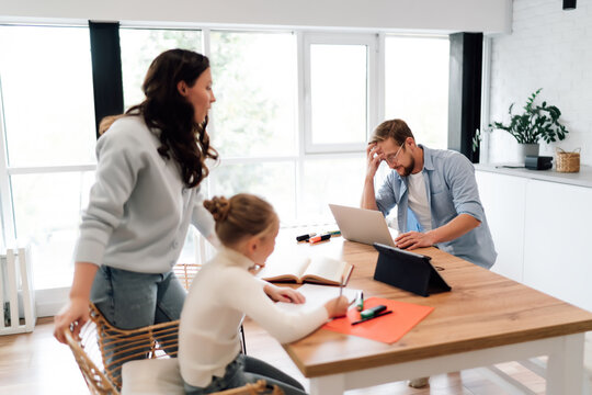 Mom, dad and daughter experience visible stress and mental load of remote work and learning, visualizing daily challenges of digital coexistence within one multifunctional household.