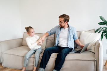 Father pauses laptop work to play with daughter, representing fluid transitions between productivity and emotional connection in a technology-embedded family space.