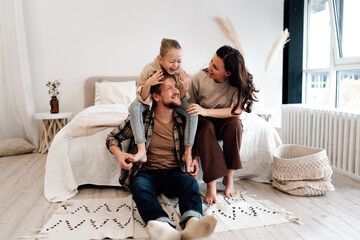 Girl giggling on dad’s shoulders while mother supports both, heartwarming family moment full of joy, playful energy, and strong emotional closeness in peaceful home space.