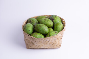 Raw green mangoes in a traditional woven bamboo basket on white background. Represents tropical fruit harvest, traditional market, healthy snack, and fresh sour taste. Food photography.
