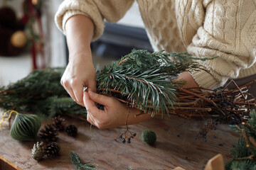 Making Christmas wreath. Hands arranging wreath with fir and cedar branches, and scissors, rustic...