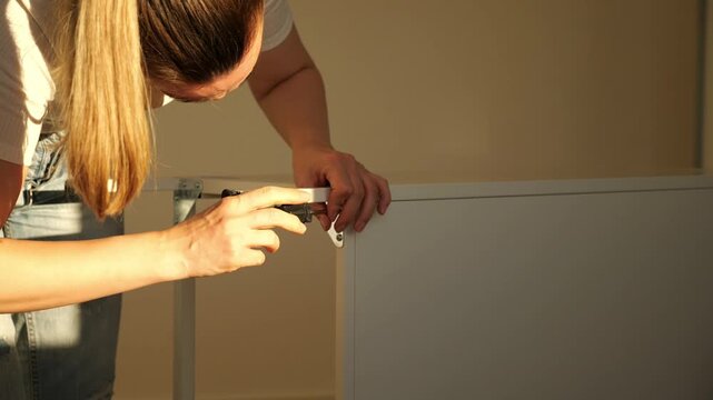 Close-up of woman&rsquo;s hands assembling flat pack furniture with screwdriver, tightening screw into wooden panel. DIY home improvement, self-assembly and modern lifestyle concept.