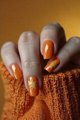 Autumn-inspired orange manicure featuring golden leaf designs on a cozy knitted background
