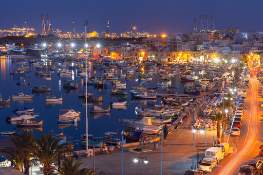 Evening view of Marsaxlokk harbor with fishing boats and waterfront lights in Malta