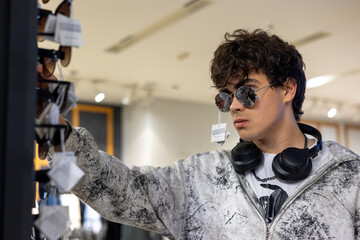 Teenager trying on sunglasses in fashion store, stylish young man shopping for accessories, youth...