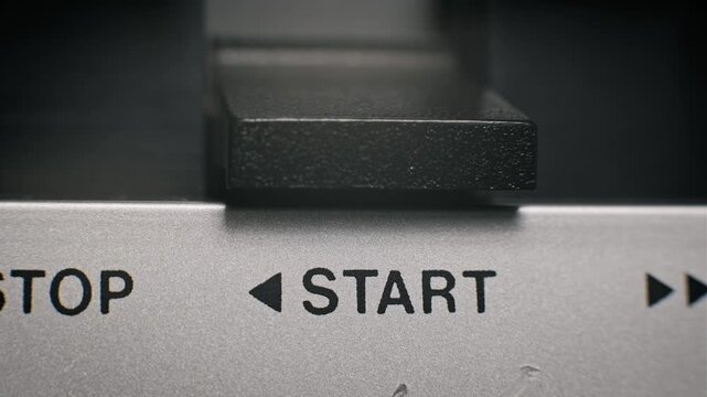 Macro perspective of a thumb pressing the black rectangular stop button on a silver brushed metal console. Clear printed typography identifies the function for operating a retro audio or video machine