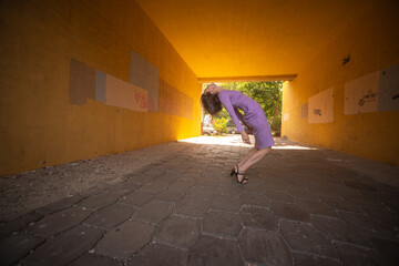 Young woman in a purple dress is joyfully jumping in a vibrant yellow tunnel, showcasing a sense of...