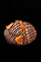 Close-up of a round cookie or small cake with dark chocolate drizzle and dried orange pieces on top, isolated on black background. Gourmet dessert, styled for food photography.