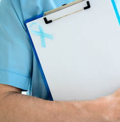 Close up of a male doctor in medical uniform holding clipboard with blue ribbon and empty sheet....