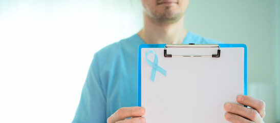 Close up of healthcare professional man holding clipboard with blue ribbon and empty form. Banner...