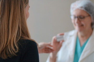 Obraz premium From behind, a nurse in white uniform hands medicine to a female patient in a hospital environment. Highlights professional healthcare, treatment plans, and patient support.