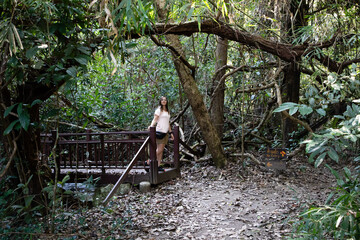 Adventurous young woman pauses on bridge amidst vibrant green forest, enjoying nature's tranquility and fresh air on a sunny day of exploration