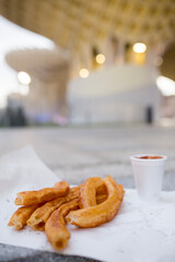 Traditional Spanish churros in Seville. The famous Metropol Parasol (Las Setas) is blurred in the background. A concept of local street food, travel, and modern architecture.