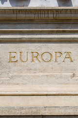 A close-up of the word 'Europa' carved in a classic serif font into a stone monument. The golden letters and weathered stone create a powerful symbol of European history and heritage.