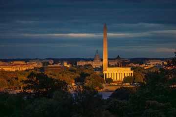 Golden sunset light bathes the Washington Monument, Lincoln Memorial, and U.S. Capitol on an autumn evening in Washington, D.C., with dramatic clouds over the National Mall.