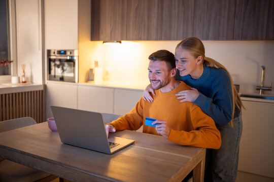 Middle-aged family couple making purchases and reservations online using laptop computer, paying by credit card. Happy man and woman reflecting contemporary digital transactions and shopping habits