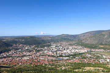 Panoramic aerial view of the city of Mostar nestled in a valley surrounded by rugged mountains and hills under a clear blue summer sky in Bosnia and Herzegovina.