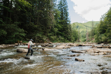 Fisherman wading in river casting line, fly fishing in mountain stream