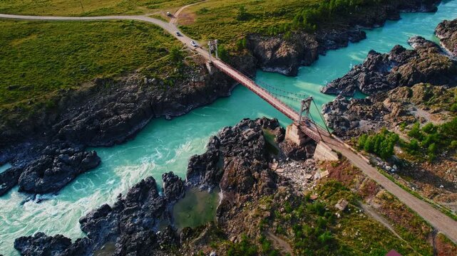Landscape suspension Oroktoysky bridge over Katun river in valley of Altai Mountains, aerial top view. Popular landmark in Chemal Siberia, Russia.