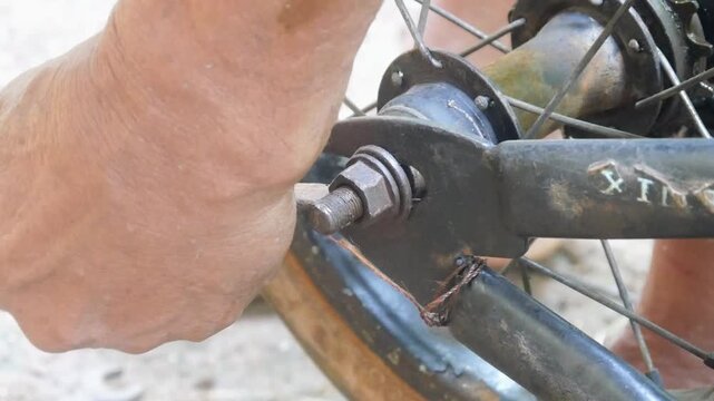 Close up of an old man's hand doing repair work on a child's bicycle wheel using a wrench.