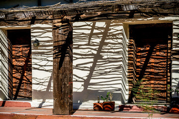 Vine coverings on a patio cover cast shadow lines on the white clay wall and doors in Tubac Arizona