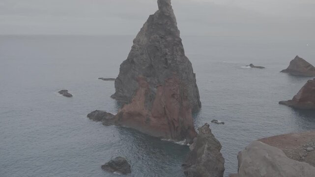 Medium shot of jagged red rock formations rising from ocean off Madeira Portugal coast (SLOG3)