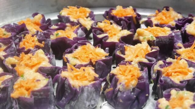 Homemade purple chicken dim sum with grated carrots on top arranged neatly on a stainless steel steamer