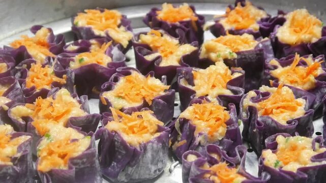 Homemade purple chicken dim sum with grated carrots on top arranged neatly on a stainless steel steamer