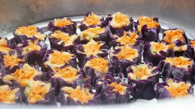 Homemade purple chicken dim sum with grated carrots on top arranged neatly on a stainless steel steamer