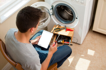 Young man consulting tablet for washing machine repair instructions at home